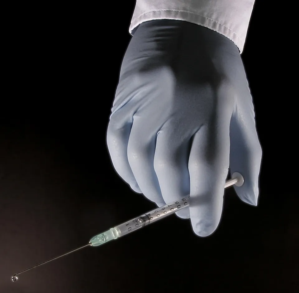 Une main gantée tenant une seringue médicale